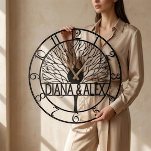 Peut inclure: Horloge murale en métal noir avec un motif d'arbre et les noms "DIANA & ALEX". L'horloge a un cadre circulaire avec des chiffres et des aiguilles dorées. Le diamètre de l'horloge est d'environ 40 cm.