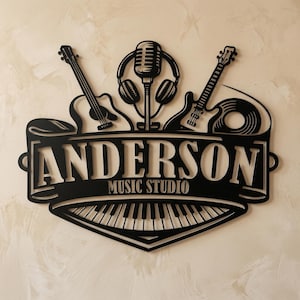 Könnte beinhalten: Schwarzes Metallschild mit dem Text "ANDERSON MUSIC STUDIO". Das Schild zeigt Silhouetten eines Mikrofons, Kopfhörern, zwei Gitarren, einer Schallplatte und einer Klaviatur. Das Schild ist an einer beigen Wand befestigt.