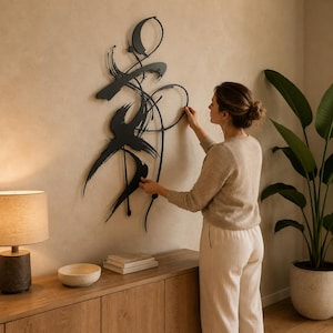 Op de afbeelding: Een zwart metalen wanddecoratie met een abstract ontwerp van vloeiende, penseelstreekachtige lijnen en cirkelvormige elementen. Het kunstwerk is opgebouwd uit dunne, onderling verbonden metalen staven en platte, gebogen vormen.