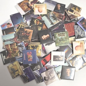May include: A large collection of assorted music CDs in plastic jewel cases, featuring various album cover art, including titles like Jackson 5 ABC, Sting, and Shawn Mendes, scattered in a disorganized pile on a plain white surface.