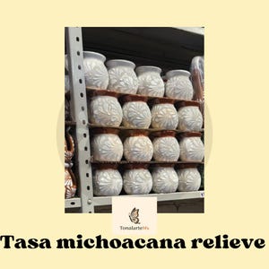 Puede incluir: Una taza de cerámica blanca con asa negra y el texto "But First, Coffee" en negrita negra. La taza se encuentra sobre un fondo borroso, sugiriendo un ambiente acogedor.