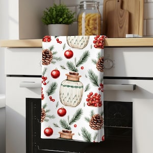 Peut inclure: Un torchon de cuisine blanc avec un motif répétitif de pommes de pin marron, de boules de Noël rouge vif, de grappes de baies rouges, d'aiguilles de pin vertes et de bocaux clairs avec des bouchons en liège, suspendu à une poignée de four.