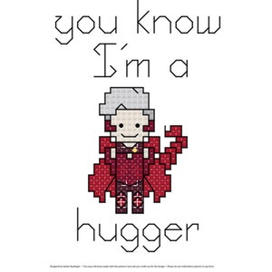 Op de afbeelding: Borduurpatroon met een cartoonfiguur met de tekst "you know I'm a hugger". Het personage is een vrouw met grijs haar, die een rode jurk en een rode cape draagt.