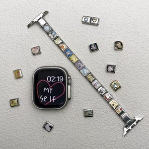 Puede incluir: Un reloj inteligente plateado con una pantalla negra que muestra "02:19" y las palabras "MY Self" dentro de un corazón rosa. Una correa de reloj plateada con dijes coloridos y dijes adicionales dispersos. La correa y los dijes son decorativos.