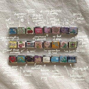 May include: A selection of silver charm bracelets with colourful designs and motivational phrases. The charms display images of flowers, hearts, and text such as "Dream Big" and "Have Fun".