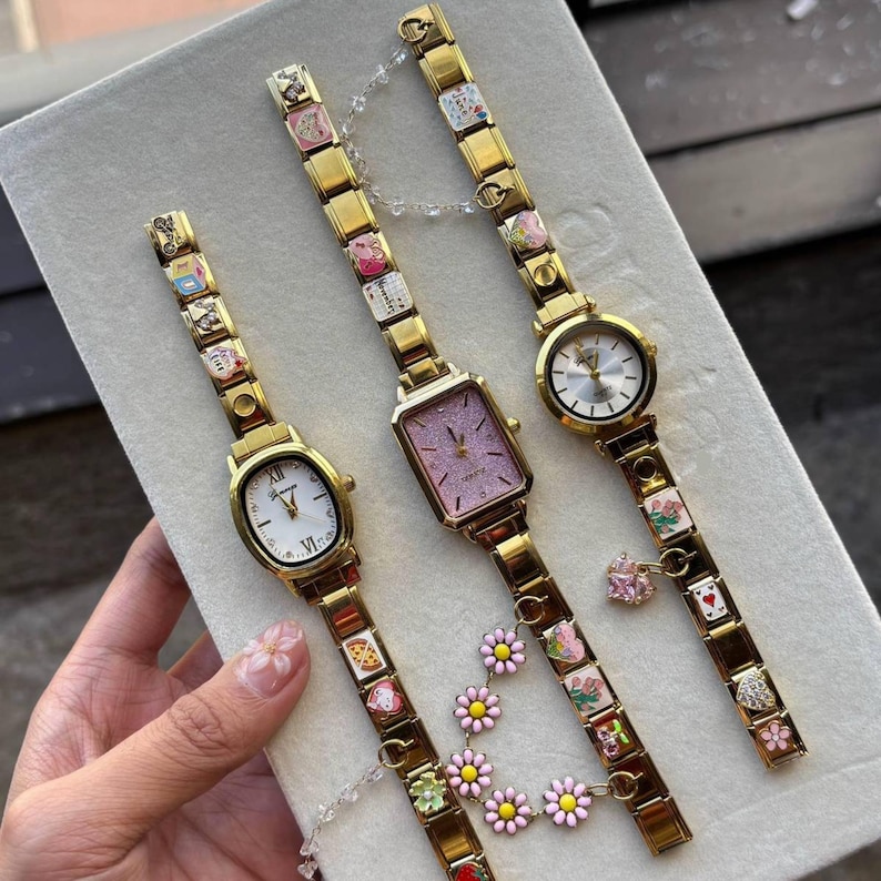 Puede incluir: Tres relojes dorados con pulseras de abalorios decorativas. Uno tiene una esfera ovalada blanca, otro una esfera rectangular rosa y el tercero una esfera redonda blanca. Las pulseras presentan abalorios coloridos y detalles florales.
