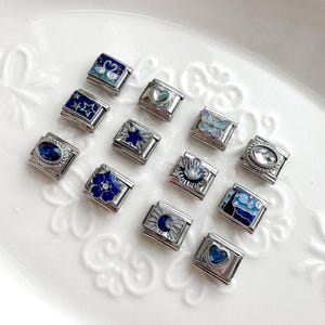 May include: A selection of silver charm bracelets with diverse designs. The charms display blue enamel patterns of swans, stars, butterflies, flowers, and hearts. Some charms have clear or blue gemstones.