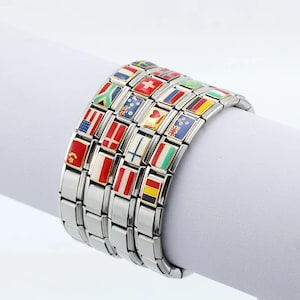 May include: A silver-toned bracelet featuring rectangular links adorned with colorful enamel flags of various countries. The flags include the United States, France, and Italy. The bracelet is displayed on a white surface.