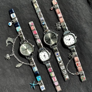 May include: Four silver charm watches with different colored charm bracelets. The watch faces are silver or white with black hands. Charms include a dolphin, starfish, and various colorful squares.