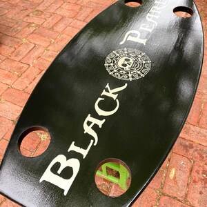 May include: Black wooden serving tray with cutouts and a white graphic of a skull and crossbones with the text "Black Pearl".