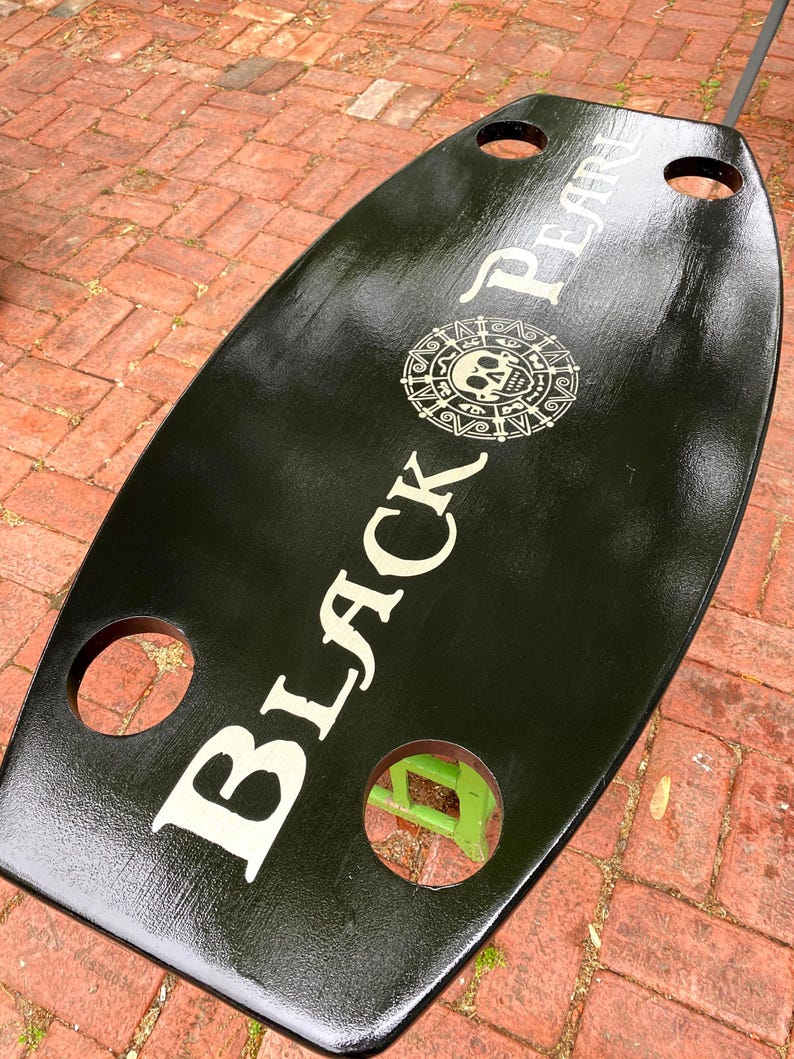 May include: Black wooden serving tray with cutouts and a white graphic of a skull and crossbones with the text "Black Pearl".