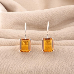 May include: A pair of silver drop earrings with rectangular, amber-coloured gemstones. The earrings have a simple, elegant design, with the gemstones set in a silver bezel and suspended from a silver hook.