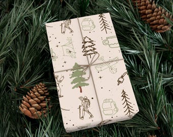 May include: A wrapped gift with a beige background and a repeating pattern of outdoor camping illustrations in green and brown. The gift is tied with twine and rests on a bed of green pine needles and pine cones.