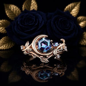Può includere: Un anello in oro rosa con una gemma esagonale centrale che cambia colore, incastonata in una forma a mezzaluna. La fascia è decorata con intricati motivi a forma di vite e foglie, arricchiti da piccole pietre trasparenti.