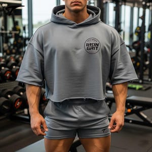 Può includere: Completo grigio composto da felpa con cappuccio e pantaloncini abbinati. La felpa ha maniche corte e orlo grezzo. La parte anteriore della felpa presenta un logo circolare nero con la scritta "IRON GRIT". I pantaloncini hanno un piccolo logo sulla gamba sinistra.
