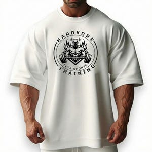 Könnte beinhalten: Weißes übergroßes T-Shirt mit schwarzem Aufdruck. Der Aufdruck zeigt eine muskulöse Figur, die Gewichte hebt, umgeben von Flammen, und die Worte "HARDKORE TETA SPORTS TRAINING" in einem kreisförmigen Design.