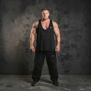 Könnte beinhalten: Eine Person in schwarzer Sportkleidung, bestehend aus einem Tanktop und einer Jogginghose. Das Tanktop hat einen tiefen Ausschnitt und ein kleines weißes Logo auf der Brust. Die Jogginghose hat ein ähnliches Logo auf dem linken Bein. Dunkelgrauer Hintergrund.