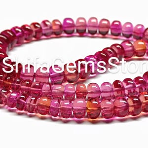 May include: Strands of translucent, barrel-shaped beads in shades of pink and red. The beads are strung together, creating a flowing, curved shape. The image has the text "ShifaGemsStore".