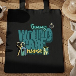 May include: Black tote bag with the text "Tammy Wound Care Nurse" in teal and white. The design includes illustrations of scissors, a bottle, a bandage roll, and a butterfly. The bag has two black handles.