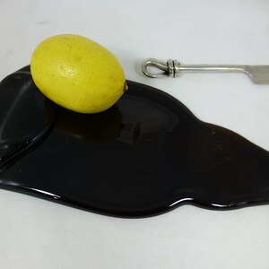 Puede incluir: Una bandeja de servir de vidrio negro con forma de botella con un limón amarillo en la parte superior.