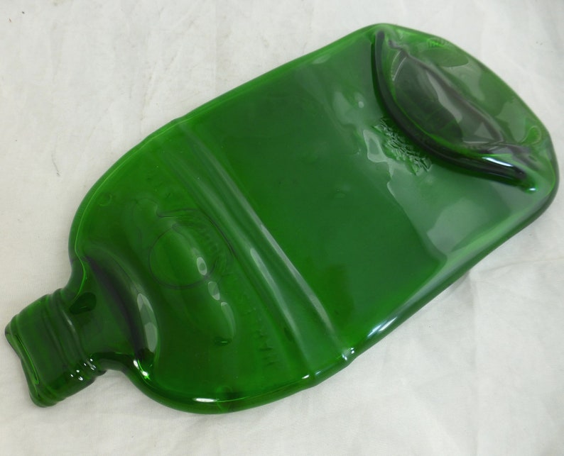 May include: A green glass bottle that has been repurposed into a serving tray. The bottle has been cut and smoothed to create a flat surface. The original label is still visible on the bottle.