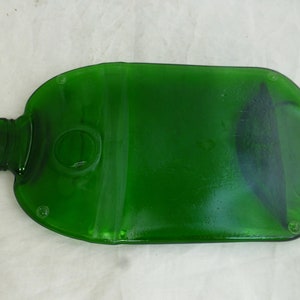 May include: A green glass bottle that has been repurposed into a serving tray. The bottle has been cut and smoothed to create a flat surface. The bottle has a round opening in the centre of the tray.
