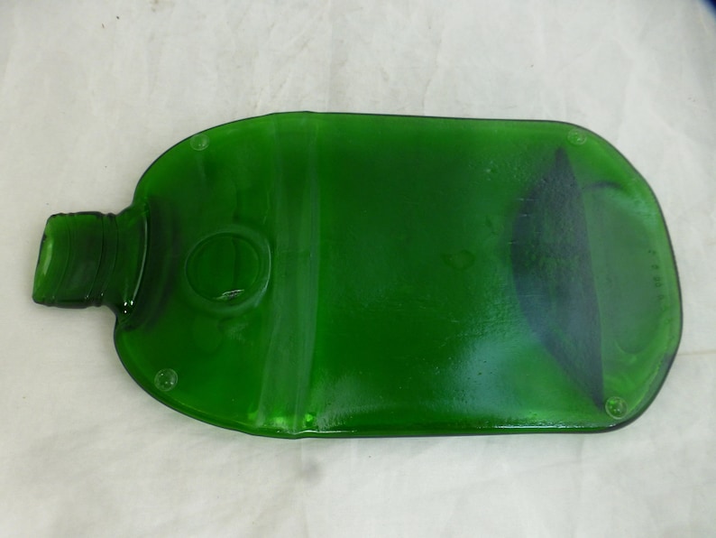 May include: A green glass bottle that has been repurposed into a serving tray. The bottle has been cut and smoothed to create a flat surface. The bottle has a round opening in the centre of the tray.