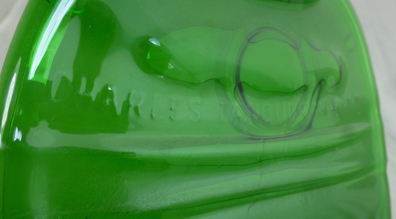 May include: A green glass bottle with a textured surface. The bottle has the words "Marles" and "Belgium" embossed on the side.