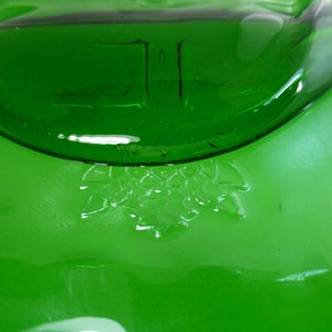 May include: Close-up of a green glass bottle with a textured surface. The bottle contains a clear liquid and has a raised design of a cluster of leaves on the bottom.