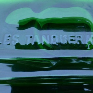 May include: A close-up of a green glass bottle with the text "CHARLES TANQUERAY & CO." embossed on the side.