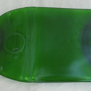 May include: A green glass bottle shaped serving tray. The tray is shaped like a bottle with a round opening in the centre. The tray has a smooth, glossy finish.