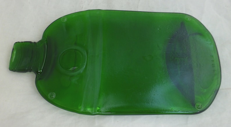 May include: A green glass bottle shaped serving tray. The tray is shaped like a bottle with a round opening in the centre. The tray has a smooth, glossy finish.