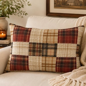 Puede incluir: Un cojín rectangular con un diseño de patchwork de cuadrados de tela a cuadros alternos en tonos rojo intenso, marrón oscuro, beige y crema. El patrón consiste en una cuadrícula de nueve cuadrados distintos con diferentes cuadros.