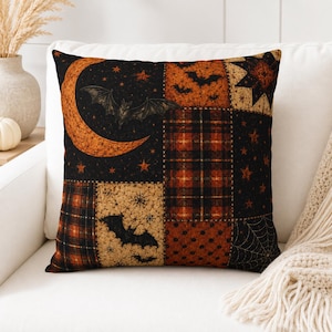 Peut inclure: Un coussin carré au motif patchwork composé de sections noires et orange. L'imprimé présente des illustrations de chauves-souris, d'un croissant de lune, d'étoiles, de carreaux, de pois et de toiles d'araignée, créant un visuel sombre.