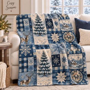 Könnte beinhalten: Eine gewebte Wohndecke mit Patchwork-Design in Blau-, Creme- und Weißtönen. Das Muster zeigt Illustrationen von Tannenbäumen, Hirschen, Schneeflocken, Nussknackern und Winterhütten, die in einem Raster aus Quadraten und Rechtecken angeordnet sind.