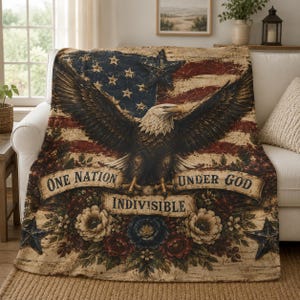 May include: A rectangular throw blanket featuring a distressed American flag background with a large bald eagle in the center. Below the eagle, a banner displays the text ONE NATION UNDER GOD INDIVISIBLE, surrounded by red, white, and blue floral accents.