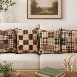 Puede incluir: Cuatro cojines cuadrados dispuestos en fila sobre un sofá. Cada cojín presenta un diseño de patchwork compuesto por varios cuadrados de tela en tonos rojo, verde, marrón y crema, mostrando una mezcla de patrones de cuadros y lisos.
