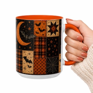 May include: A ceramic mug with a bright orange interior and handle, featuring a black and orange patchwork pattern on the exterior. The design includes motifs of bats, a crescent moon, stars, plaid squares, polka dots, and a spider web.