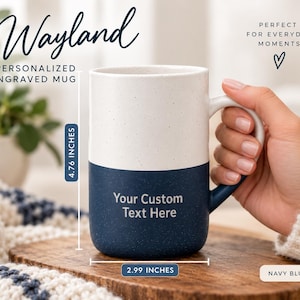 May include: A two-toned ceramic mug with a speckled white top and a solid navy blue bottom. The mug features the engraved text 'Your Custom Text Here' on the navy section. It measures 4.76 inches in height and 2.99 inches in width.