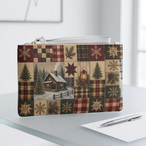 May include: A rectangular wristlet pouch featuring a patchwork design of winter scenes, including a snow-covered log cabin, pine trees, snowflakes, pinecones, and plaid patterns in shades of red, green, brown, and cream with a white wrist strap.