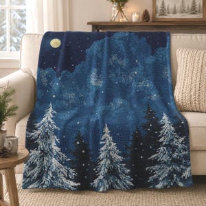 May include: A soft throw blanket featuring a dark blue night sky with a yellow moon and scattered stars above a forest of snow-covered evergreen trees. The design has a textured appearance with deep blue, white, and black colour tones.