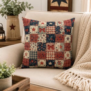May include: A square throw pillow featuring a patchwork design of red, white, and blue fabric squares. The pattern includes various motifs such as five-pointed stars, plaid checks, floral prints, and small bows arranged in a grid across the surface.