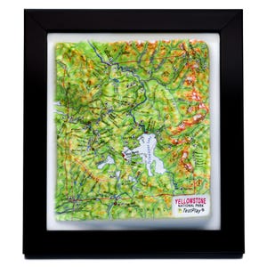 Könnte beinhalten: Eine gerahmte Karte des Yellowstone-Nationalparks, Wyoming, mit 3D-Topografie-Effekt. Die Karte zeigt grüne, gelbe und braune Geländedetails mit blauen Linien, die Flüsse und Seen darstellen. Der Rahmen ist schwarz, und die Karte enthält den Text "Yellowstone National Park".