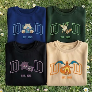 May include: Four crewneck sweatshirts in navy blue, dark green, black, and tan. Each features a "DAD" design with a different cartoon character and the text "EST. 2025" or "EST. 2018". The sweatshirts are laid out on a bed of grass.