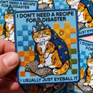 May include: Square patch featuring an orange tabby cat wearing a wizard hat and cape, sitting on a book. Text reads "I DON'T NEED A RECIPE FOR DISASTER" and "I USUALLY JUST EYEBALL IT". The background is blue and orange.