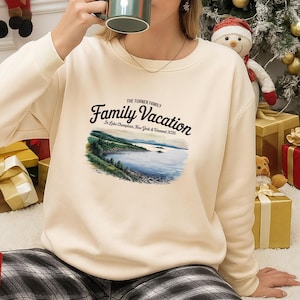 May include: Cream-colored sweatshirt with the text "Family Vacation" above a scenic lake illustration. The text also includes "The Turner Family" and "In Lake Champlain, New York & Vermont 2026". The sweatshirt has a crew neck and ribbed cuffs.