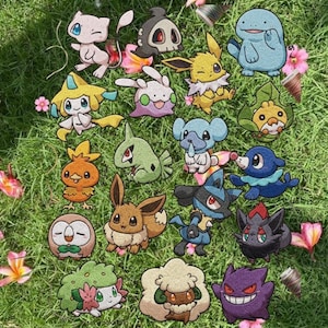May include: A collection of colorful embroidered patches featuring various cartoon characters, including a light pink cat, a blue elephant, and a purple ghost. The patches are arranged on a bed of green grass with pink flowers.