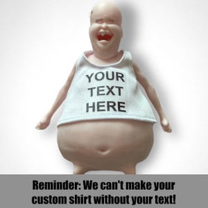 May include: A novelty figurine with a bald head and a wide, laughing mouth, wearing a white tank top. The tank top has the text "YOUR TEXT HERE" printed in black. The image also includes the text "Reminder: We can't make your custom shirt without your text!"