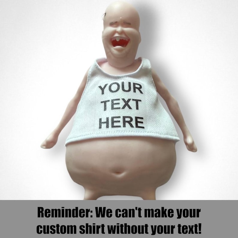 May include: A novelty figurine with a bald head and a wide, laughing mouth, wearing a white tank top. The tank top has the text "YOUR TEXT HERE" printed in black. The image also includes the text "Reminder: We can't make your custom shirt without your text!"