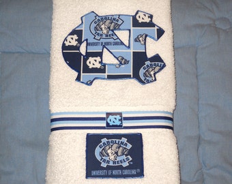 Può includere: Asciugamano da bagno bianco con un logo blu e bianco Carolina Tar Heels. Il logo è una grande 'C' blu con una 'N' blu più piccola all'interno. L'asciugamano ha un nastro blu e bianco attorno.